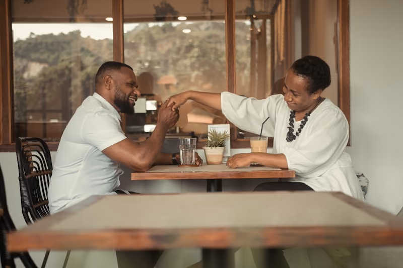 Two people at a cafe table, hands clasped over the table, laughing