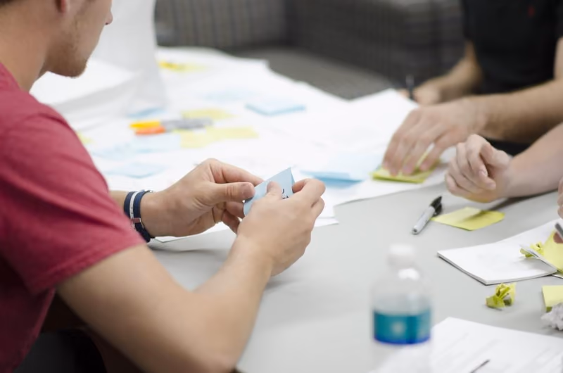 A hand sorting coloured sticky notes across a cafe table