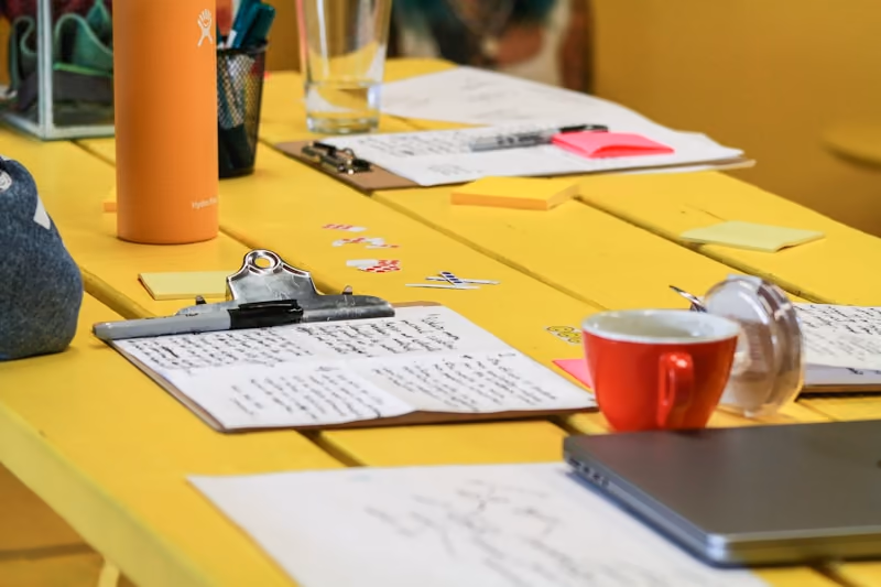 Handwritten planning sheets, a mug and a laptop spread across a yellow table